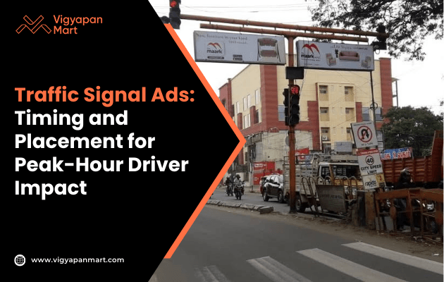 Street view of a traffic signal with advertisements on overhead boards. Vehicles wait at the red light, with a building and trees in the background.